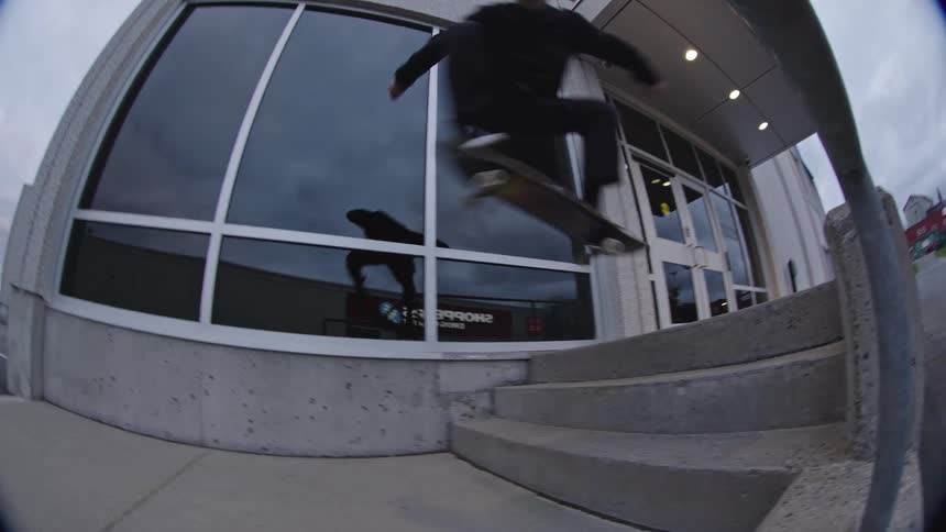 A teenage boy is skateboarding off some steps into a parking lot
