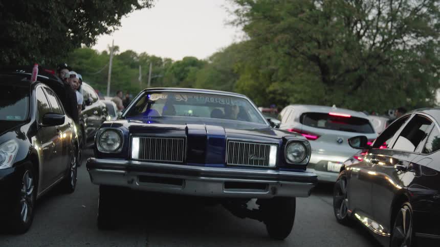 A lowrider bouncing while passing by people watching and other cars