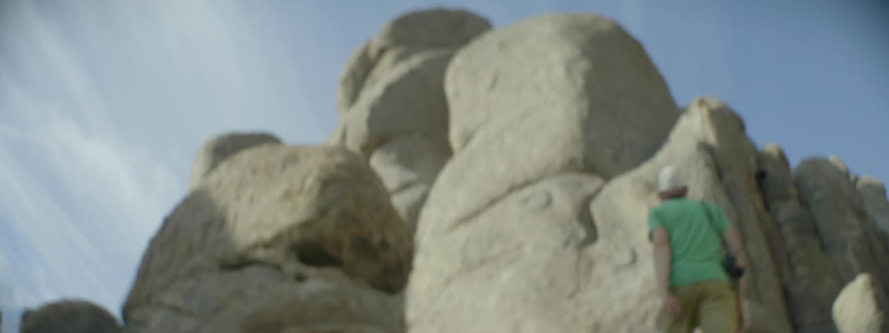 Man with camera hiking up large boulders in wilderness on sunny day