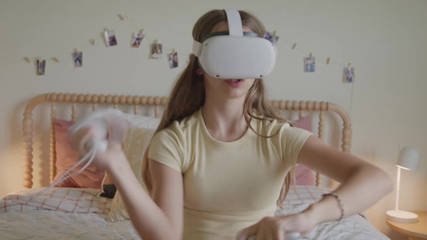 The teenager sits in bed using a vr headset with controllers