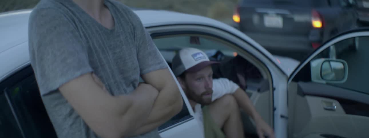 A man and woman talk by a car at sunset