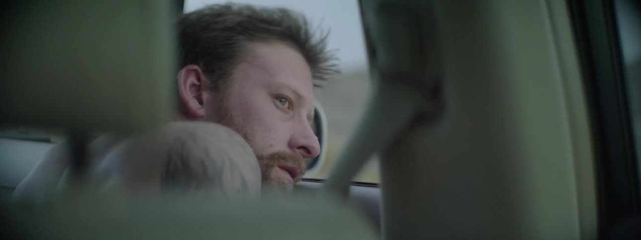 A man leans out the window of a moving car