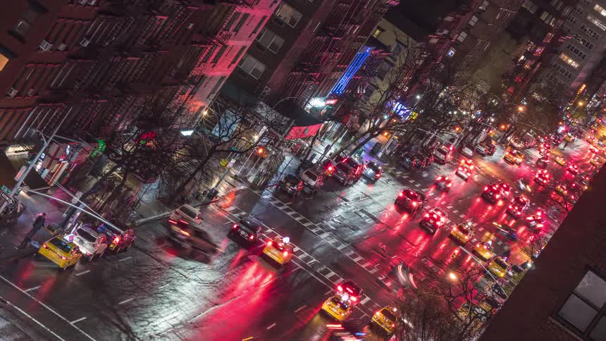 The video is a highangle shot capturing the vibrant highdensity street traffic in a city at nightthe wet streets reflect the red brake lights and yellow headlights of cars and taxis creating a streaked dynamic effect on the pavement