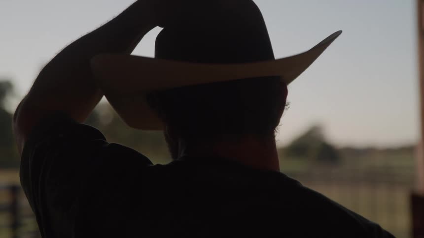 Man standing on a rural homestead puts on his cowboy hat