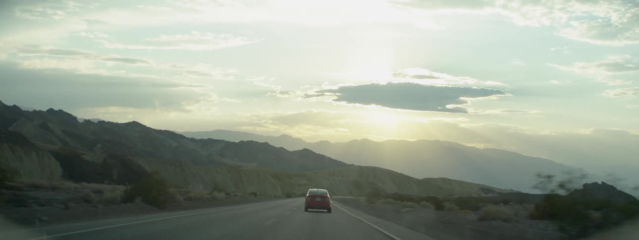 Car traveling on mountain highway while sun sets behind clouds