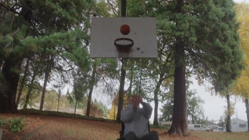 The young man in a wheelchair is playing basketball on friday and then celebrates with his arms out to the sides