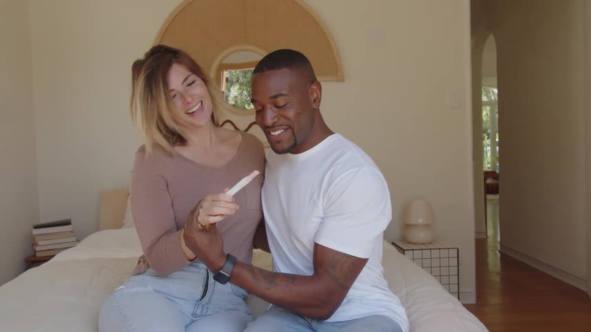 Excited couple sitting on bed holding a postive pregnancy test