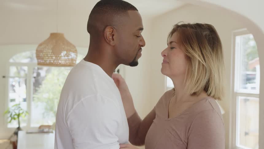 The video opens with a closeup shot of a black man and a white woman smiling at each other in a brightly lit modern homethe couple then embraces showing a brief and tender moment of interracial affection and connection