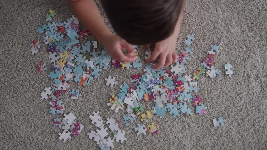 A young boy sorts through puzzle pieces scattered on the carpet
