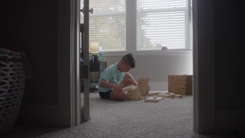 Boy sitting on the floor stacks wooden pieces from a construction set during the daytime