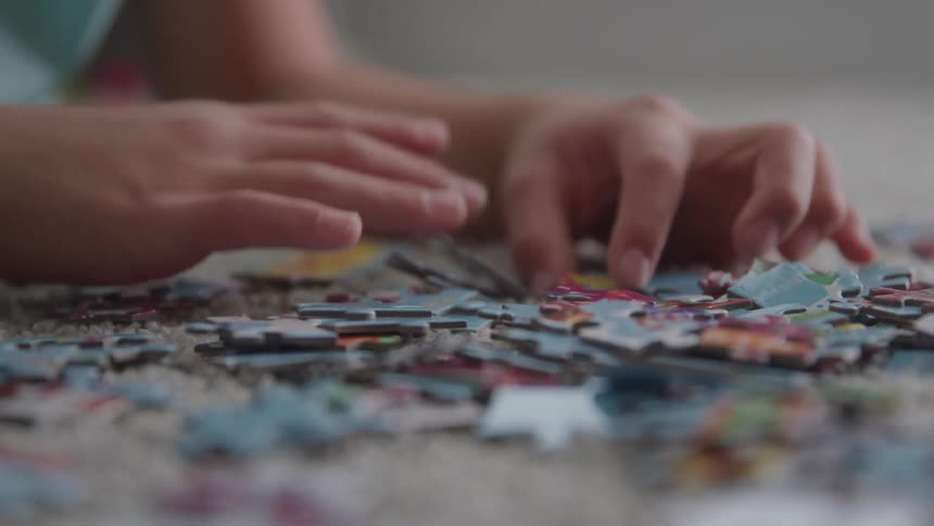 Child inspects the pieces of a jigsaw puzzle while lying on the floor