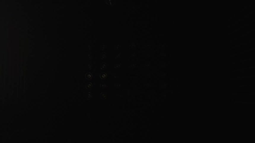 Multiple bright circular lights flash on and off in various patterns in a dark hazy room briefly illuminating a silhouetted figure standing in the center