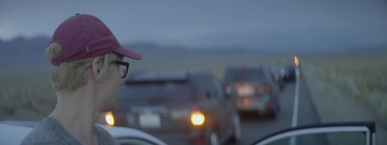 A man leans against a car while traffic is backed up and stopped