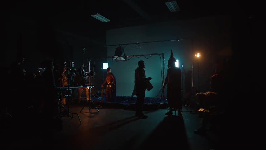 Film crew shooting a scene with actors in costume on a dimly lit set