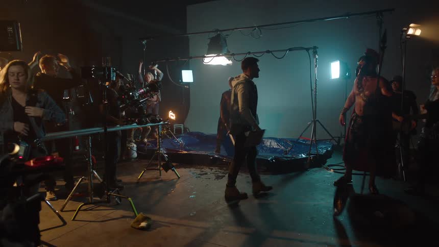 The video shows a behindthescenes look at a film or stage production set in a dark rooma group of people possibly the crew are manipulating a large flamethrowing prop which is being used to simulate a fire in the foreground