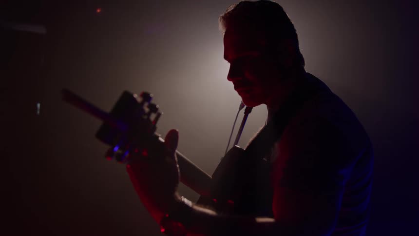 The man is playing guitar on the dark stage