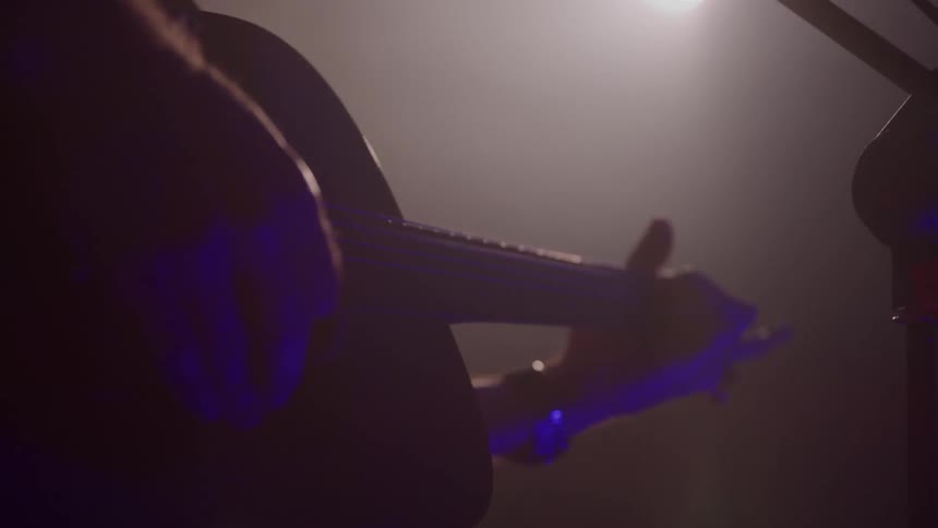 A closeup of a musician playing a guitar under stage lighting