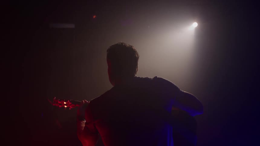 Man plays a guitar while performing on stage under a spotlight
