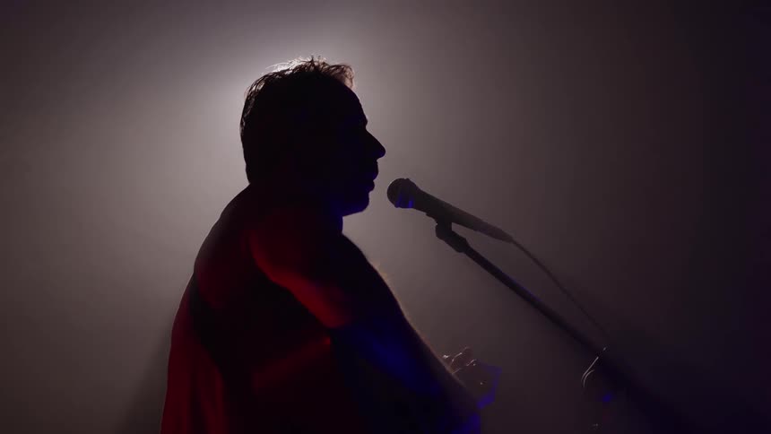 A man strums on a guitar while singing into a microphone on stage