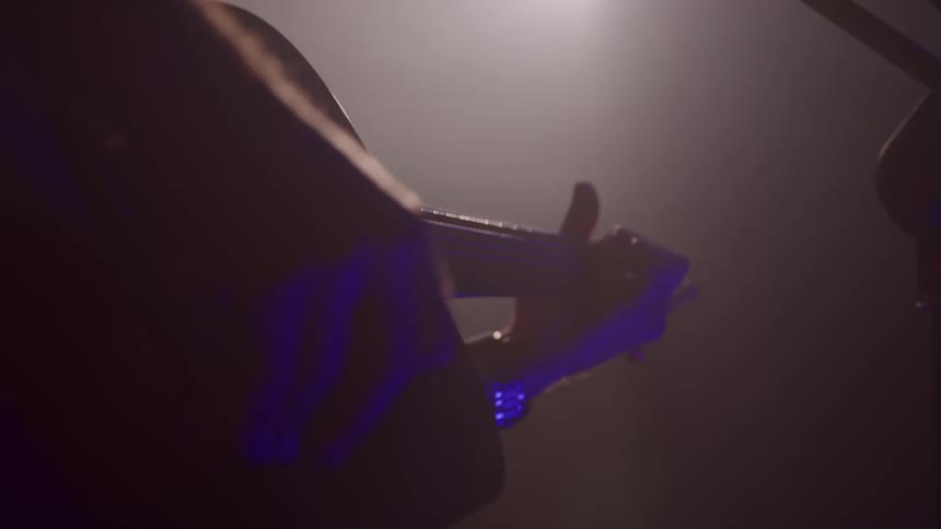 The man is performing on the dark stage with a guitar