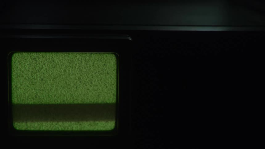 A small green monitor glows in the darkness its screen filled with flickering static and a rolling glitch before it suddenly turns off