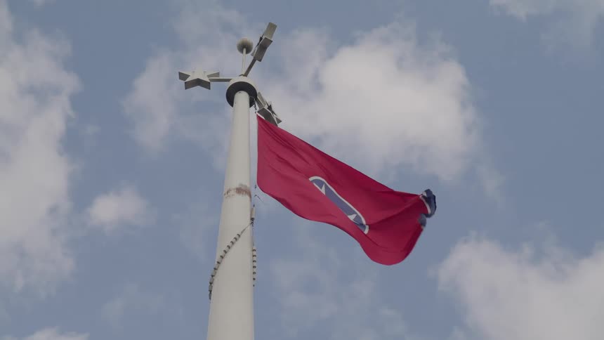 A low angle shot shows the red flag of tennessee whipping in the wind on a tall white flagpole against a cloudy blue sky