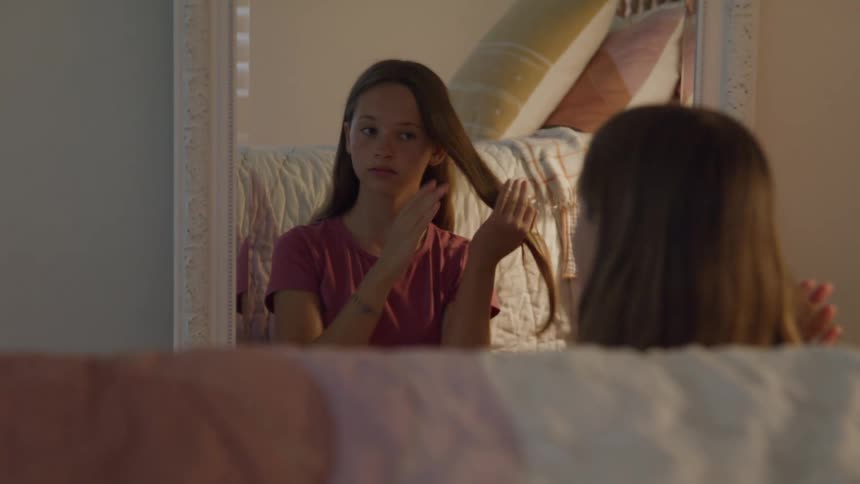 Young girl standing in front of mirror fixing her long hair