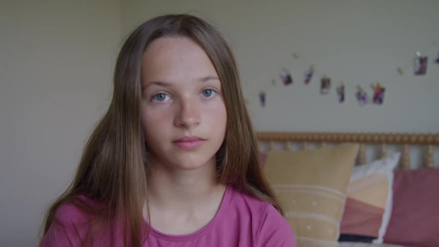 Young girl sits on her bed and faces forward