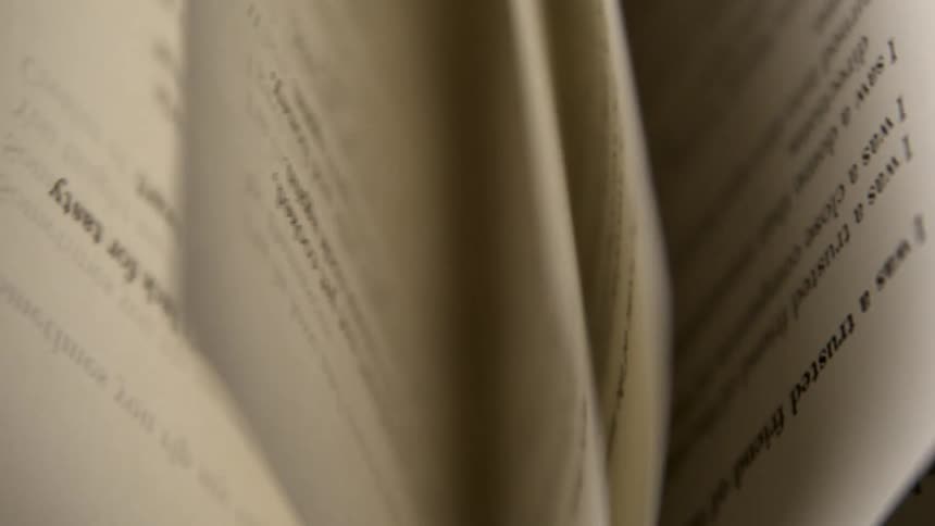 An extreme close view shows the pages of an open book being flipped through with printed text visible on the yellowed paper
