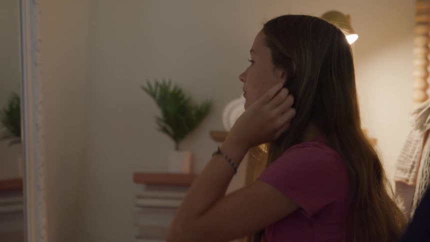A female teenager arranging her hair while sitting in front a mirror in a room