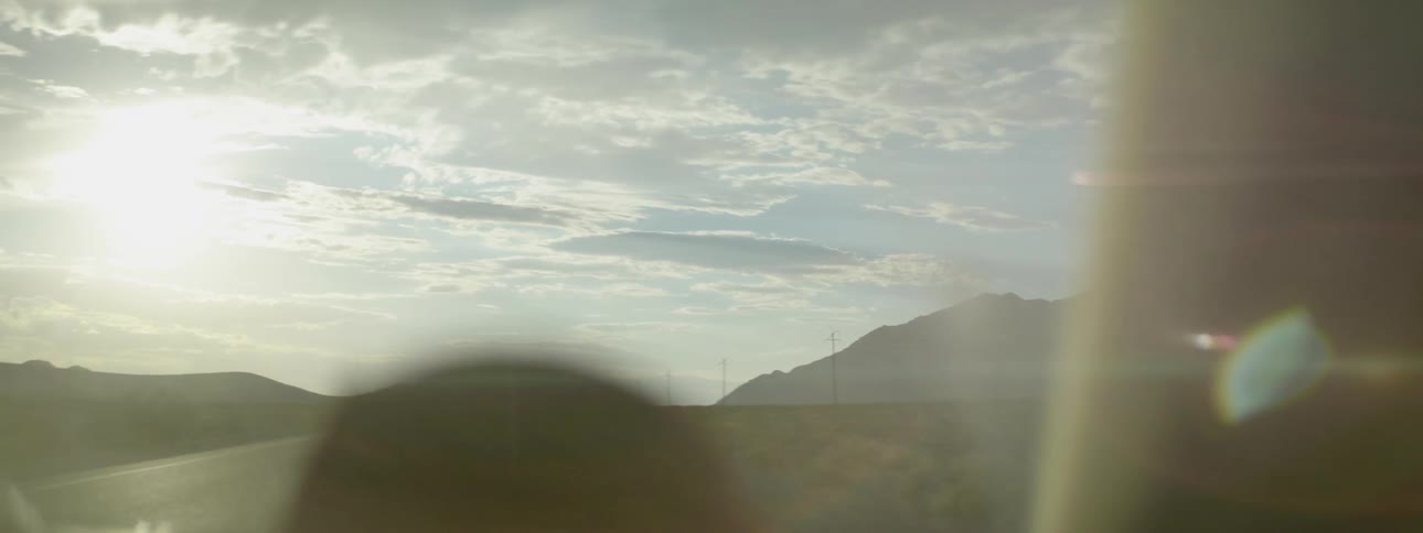 A vehicle drives with mountains and clouds in the distance