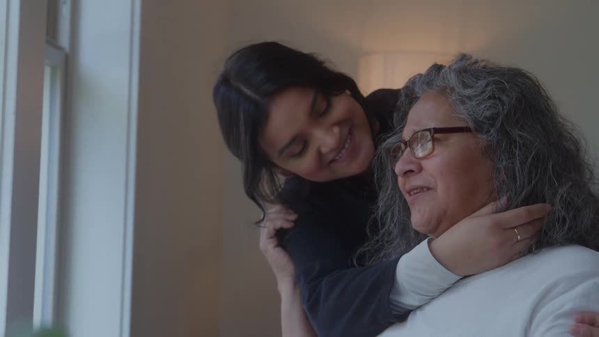 A younger female is hugging and stroking the hair of an older female in a room