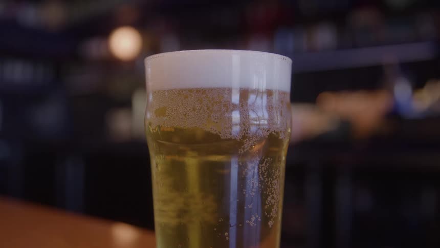 A pint glass filled with amber beer is sitting atop a bar counter