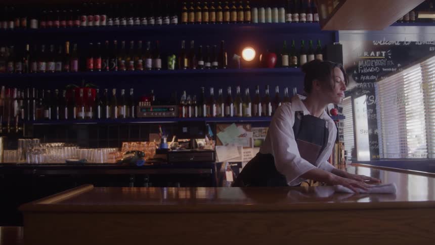A bartender in an apron cleans the bar countertop after a party