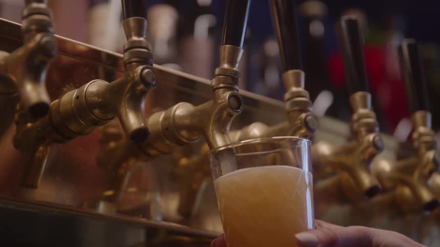 A person holds a pint glass below a tap and fills it with beer