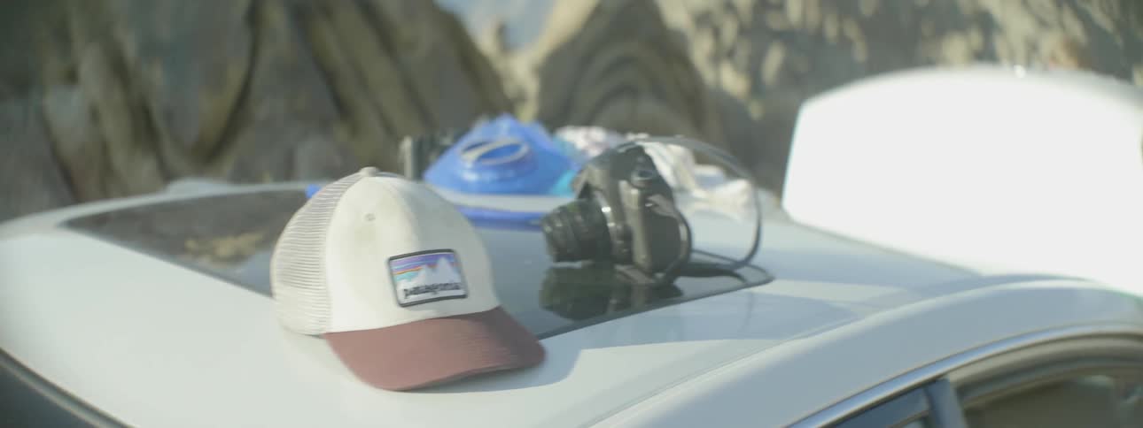 Hat and camera sitting on roof of car with its hood open