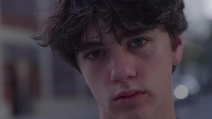The face of a teenage boy who was looking down and then starts looking forward with a sad look