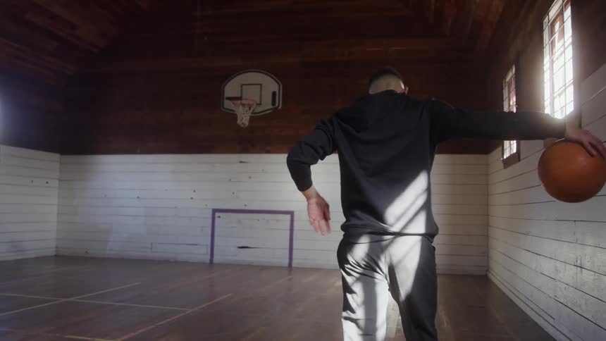 A young man playing basketball in an indoor court during daytime