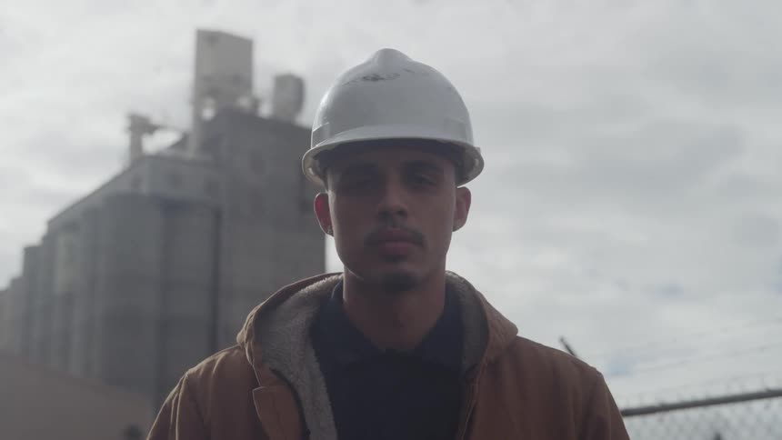 Man stands with an industrial silo behind him under a bright sky