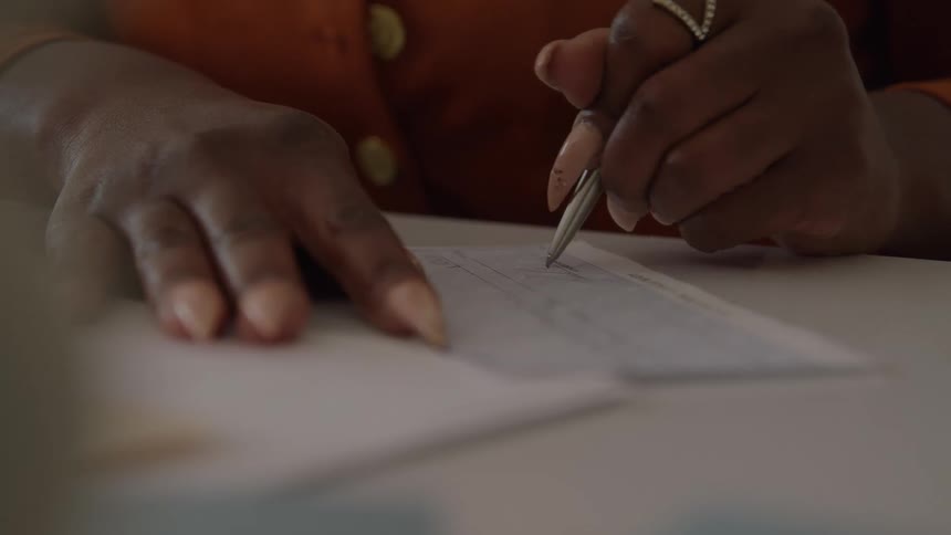A persons hand using a silver pen to write on white paper