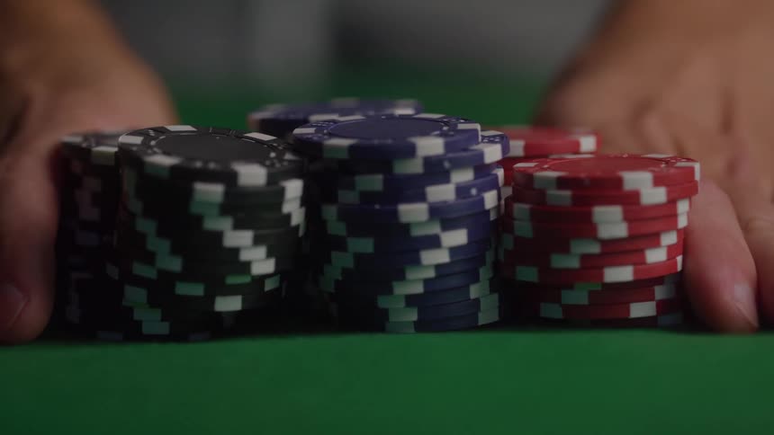 A closeup shot focuses on multiple stacks of colorful poker chips placed firmly on a green felt casino table hands slightly out of focus push the large bet forward as the camera racks focus onto the chips
