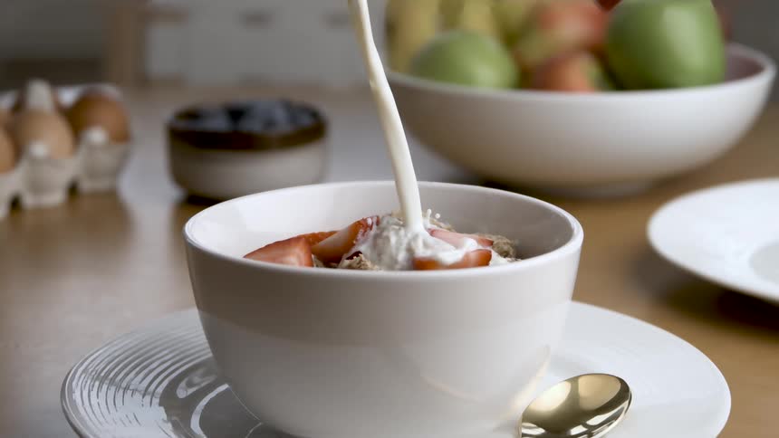 Milk pouring over cereal and strawberries in a white bowl