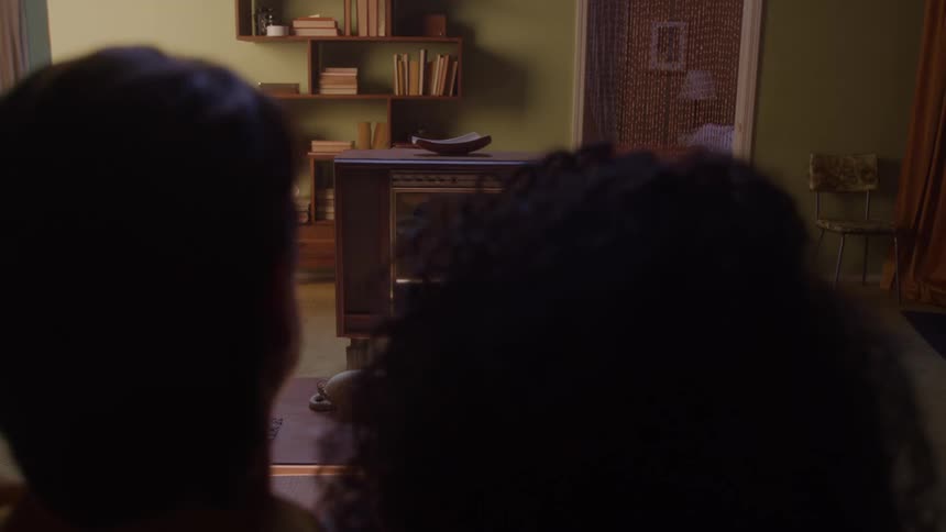 Two people cuddling on a sofa turning on an old television in a living room