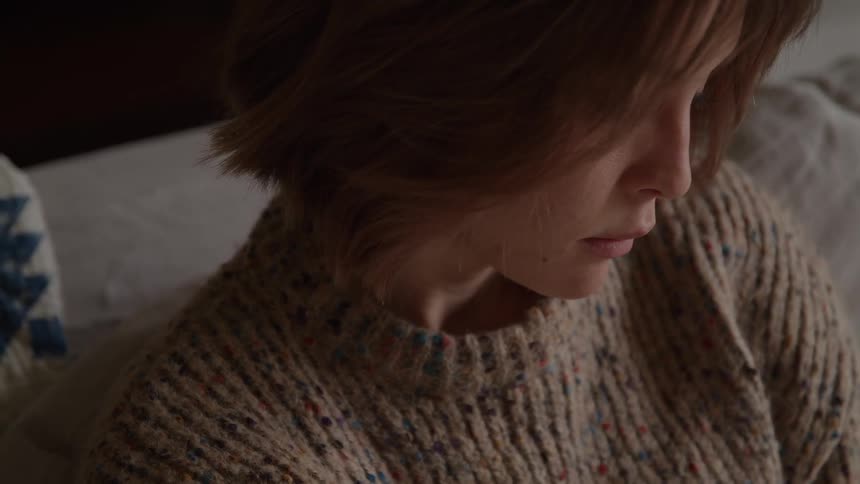 The face of a young woman with short hair and wearing a sweater who is looking at something below