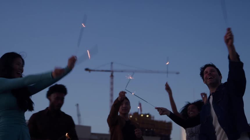 Group of friends holding sparklers and celebrating outdoors at dusk