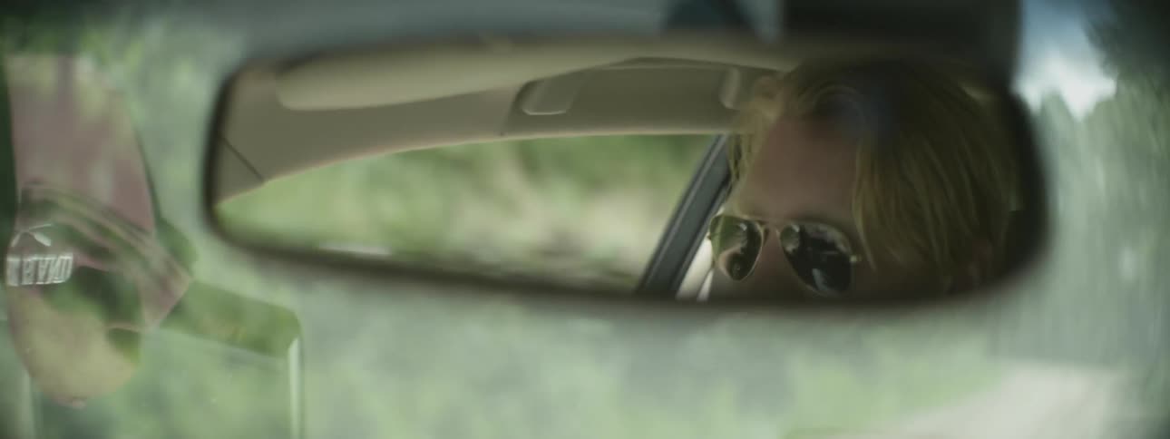 A driver's reflection is shown in the rearview mirror