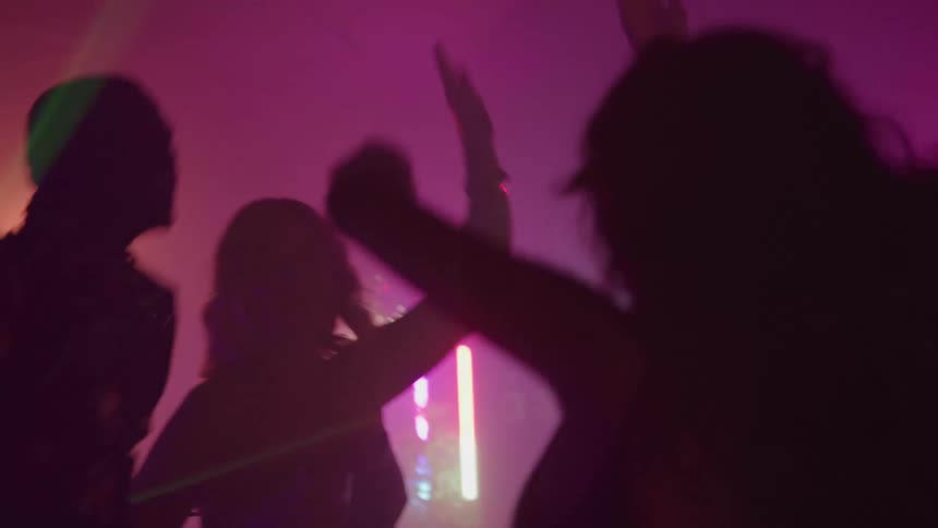 The video shows the silhouettes of several people dancing in a dimly lit space likely a club or party they are raising their arms and moving to the music against a backdrop of shifting pink and purple lights