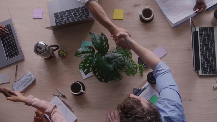 Business people shake hands over a conference table in an office