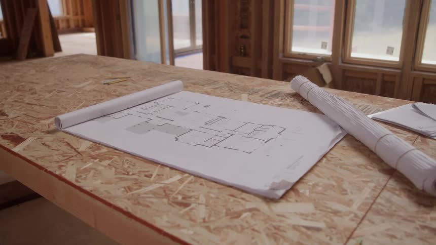 Unrolled floor plan lies on a piece of plywood in a building under construction during the daytime