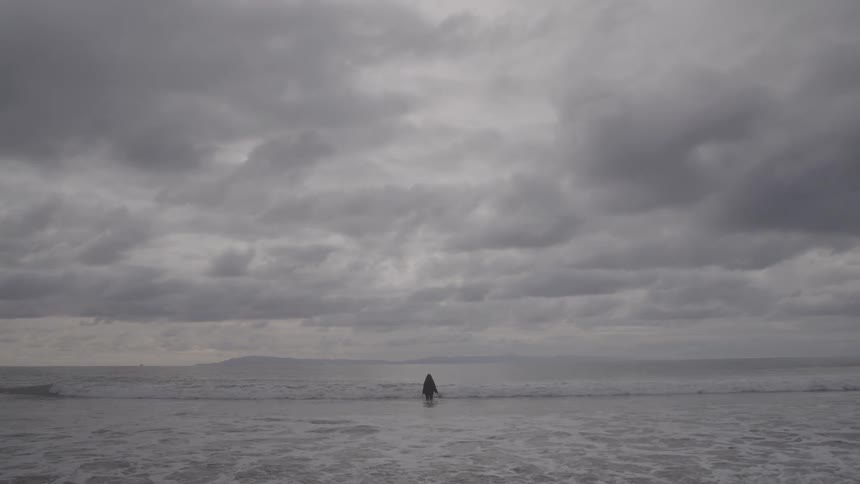 A clothed person is standing in the ocean water near the beach